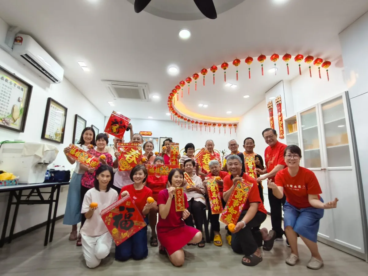 学员与长青班同修手持春联与柑橘,在挂满红灯笼的课室合影