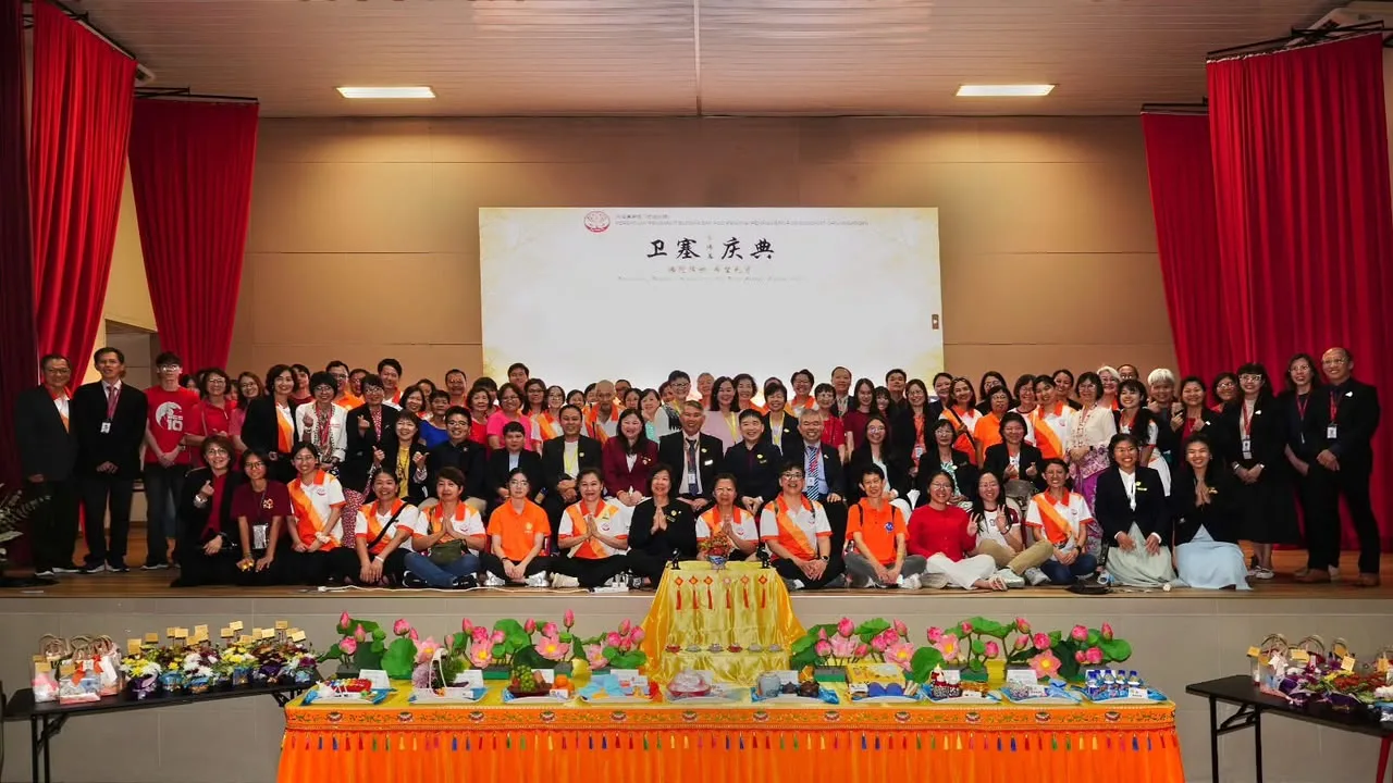 卫塞庆典大合照,学员与义工在礼堂舞台上合影,台前供满莲花与供品